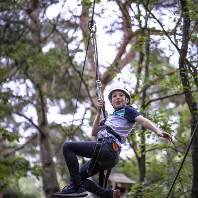 A boy hanging from a zip wire at Wild Pines Park.
