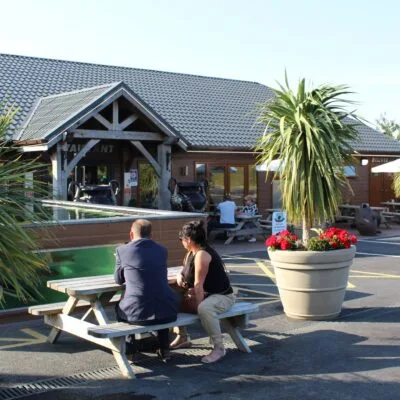 exterior view of a resturant on a lake with people sat outside