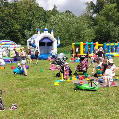 Families playing on inflatables and sitting on grass at Funtopia event.