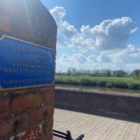 A blue plaque on a wall over looking riverside walk