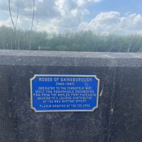 A blue plaque mounted on a wall that reads: "Roses og Gainsborough (1880 - 1987) Dedicated to the townfolk who built this remarkable engineering firm. From the world's first packaging machine to a leading contributor of the WW2 wartime effort. Plaque erected by the Delvers.