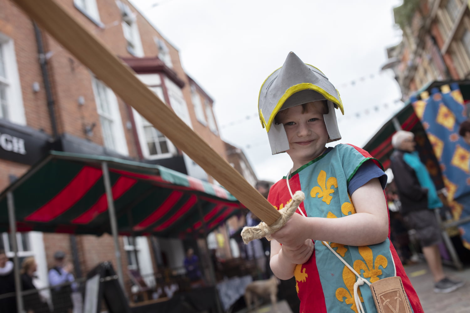 Boy dressed as a knight holding a wooden sword.