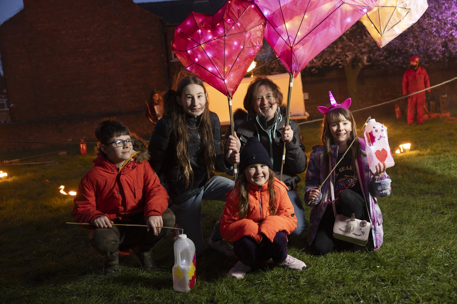 Family holding 2 large lanterns and homemade lanterns in the Fire Garden at Illuminate 2024