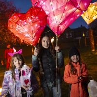 Girl holding 2 large heart lanterns and 2 girls holding homemade lanterns in the Fire Garden at Illuminate 2024