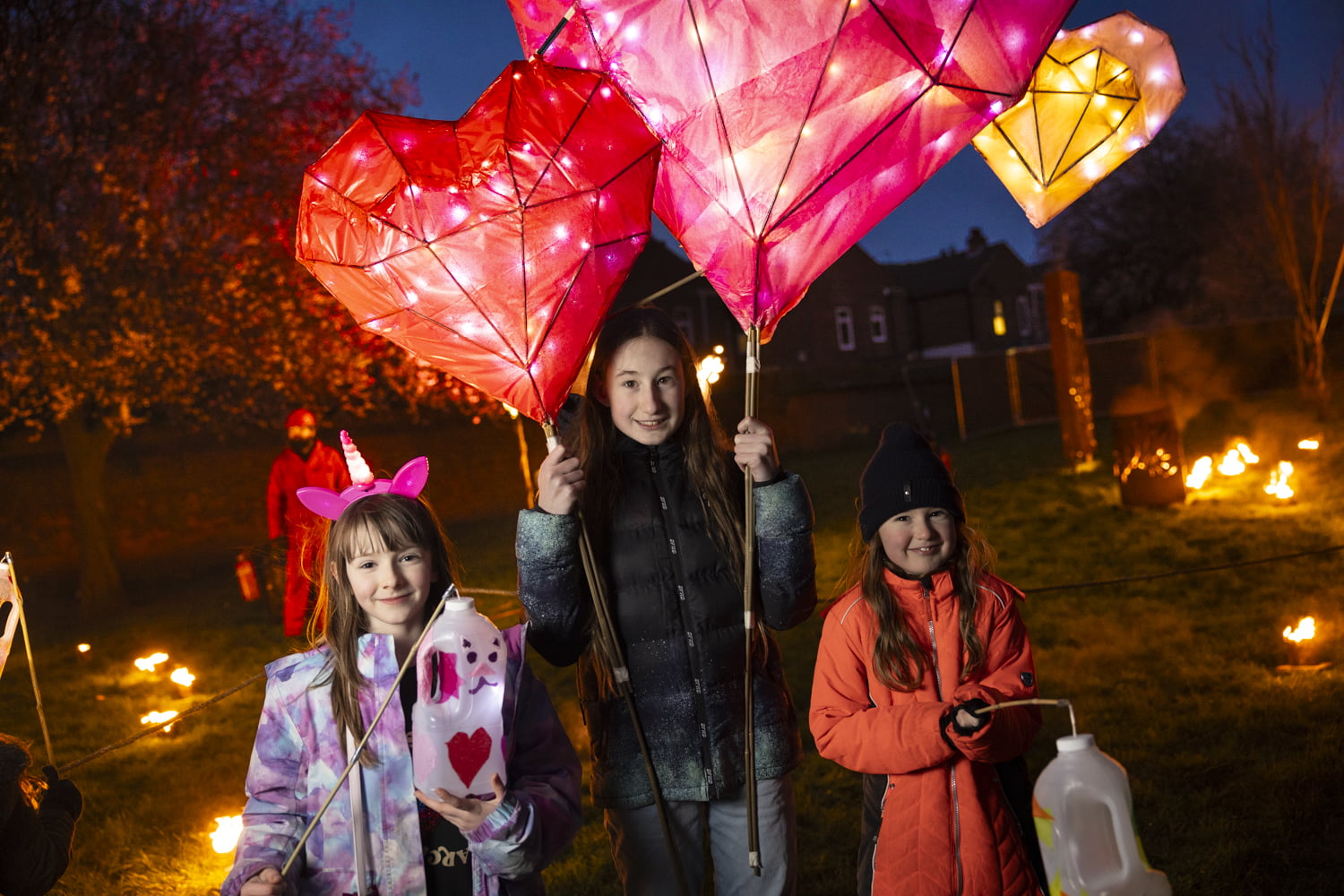 Girl holding 2 large heart lanterns and 2 girls holding homemade lanterns in the Fire Garden at Illuminate 2024