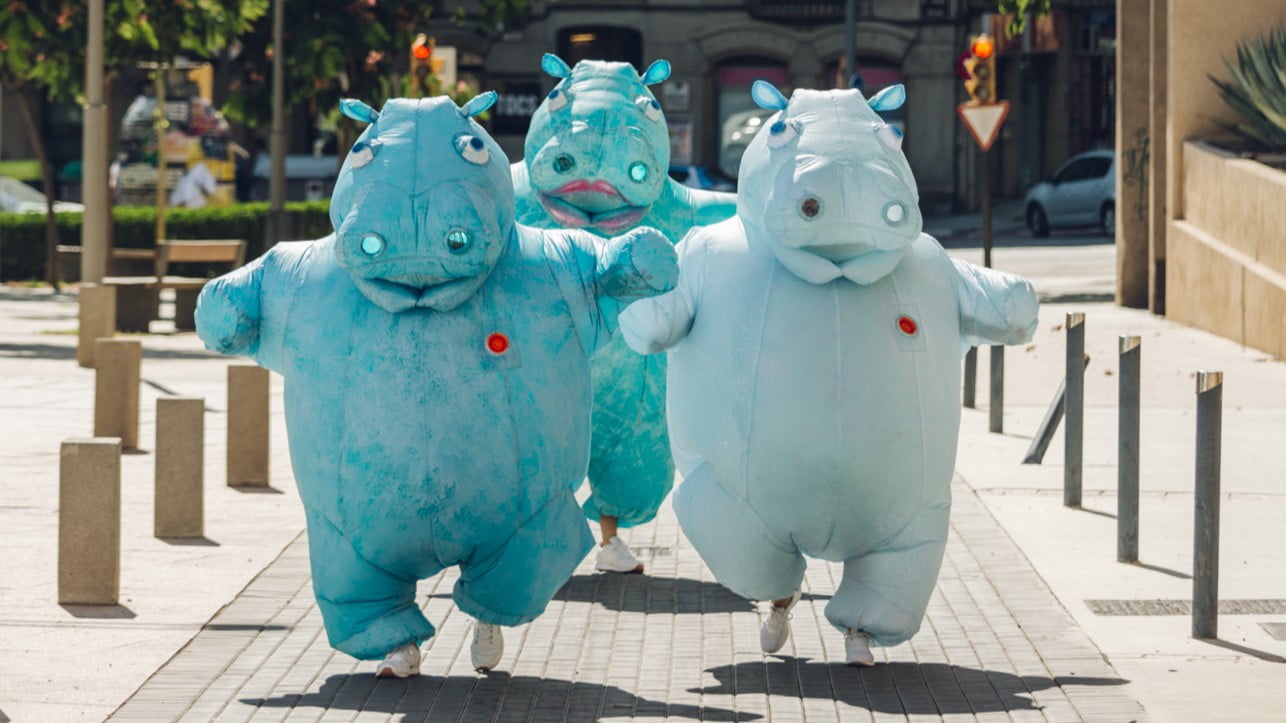 Three people dressed as large hippos