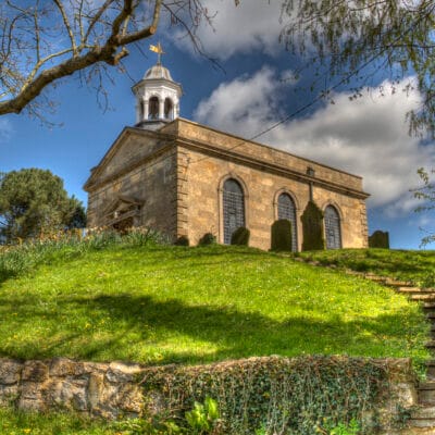 Achurch on a hillside with a green bank in front and a blue sky behind