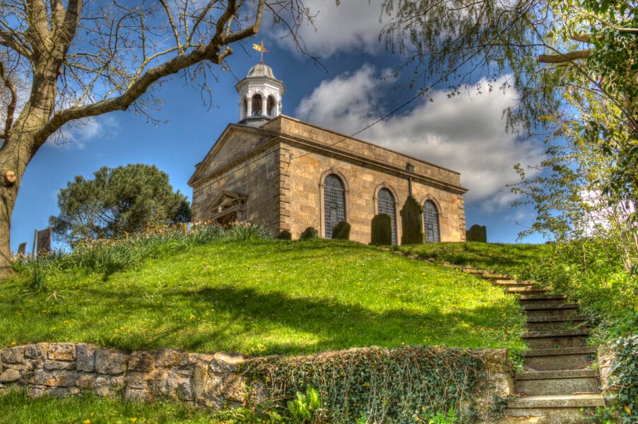 Achurch on a hillside with a green bank in front and a blue sky behind